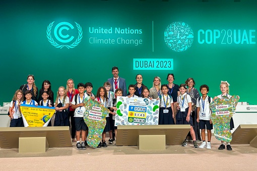 Group of children and grown ups holding Green Footprints campaign sign at COP28 in Dubai